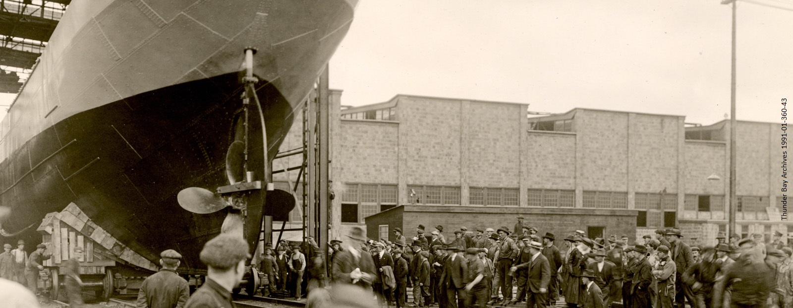 black and white photo of boat moving down rails with people looking on