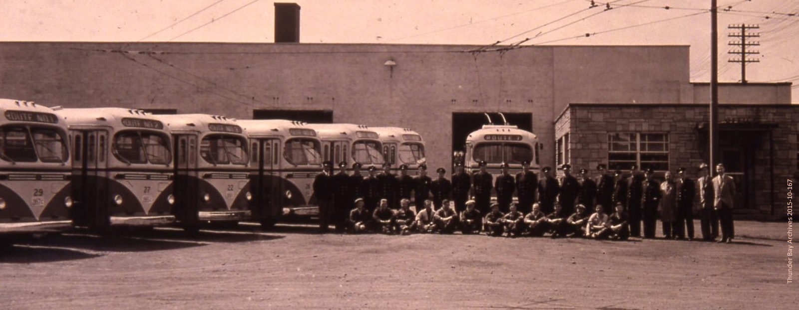 A group of transit drivers standing in front of buses parked at a garage