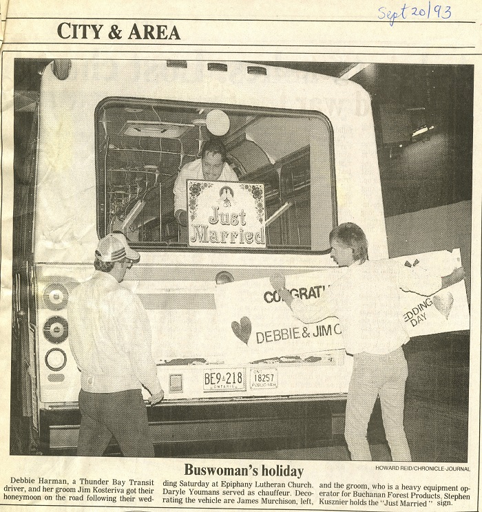 A newspaper article showing a photo of two people affixing a sign to the front of a bus