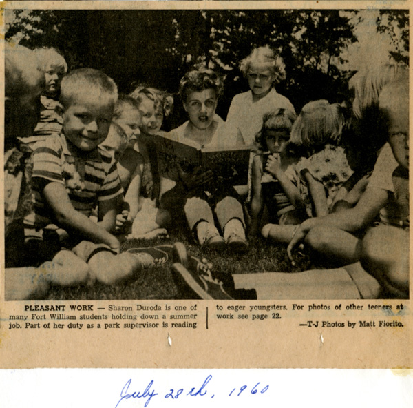 A group of children gathering around an adult holding a book
