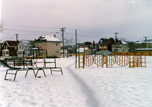 Snow blanketing the ground with a play structure in front and houses behind