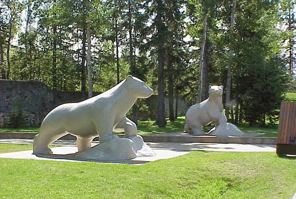 Two polar bear statues sitting in grass with trees and pathways
