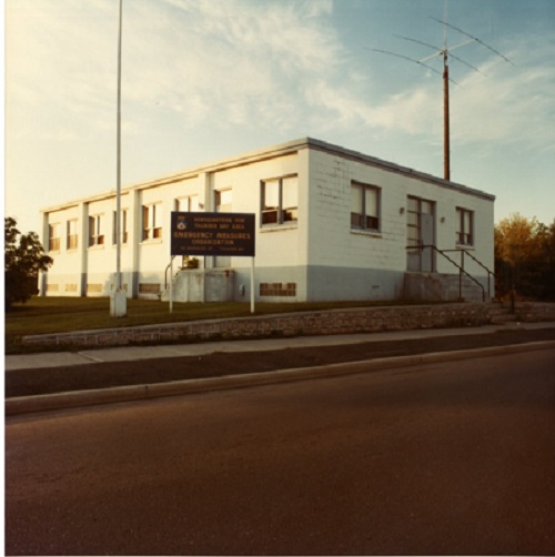 A white building with a brown and yellow sign saying Emergency Measures Organization