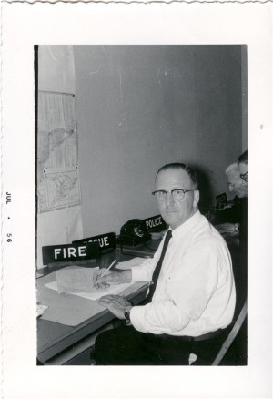 A man sitting at a desk wearing a white shirt and tie 