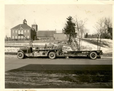 A firetruck sitting in front of a vacant field with a building farther back