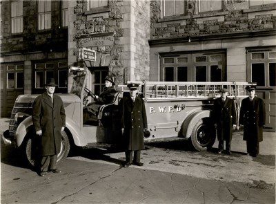A group of firefighters standing in front of a truck parked in front of a building