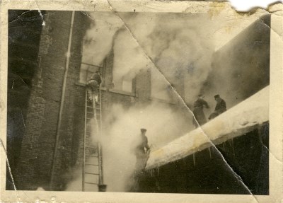 A black and white photo of Firefighters battling a fire in winter
