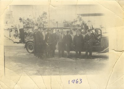 A group of firefighters standing in front of a fire truck, picture is very faded