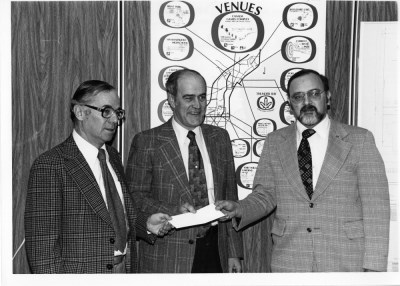 Three men stand together in front of a banner 