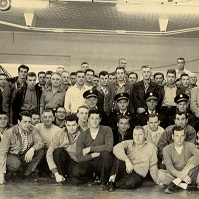A group of men standing together in a fire hall, with a firetruck behind them