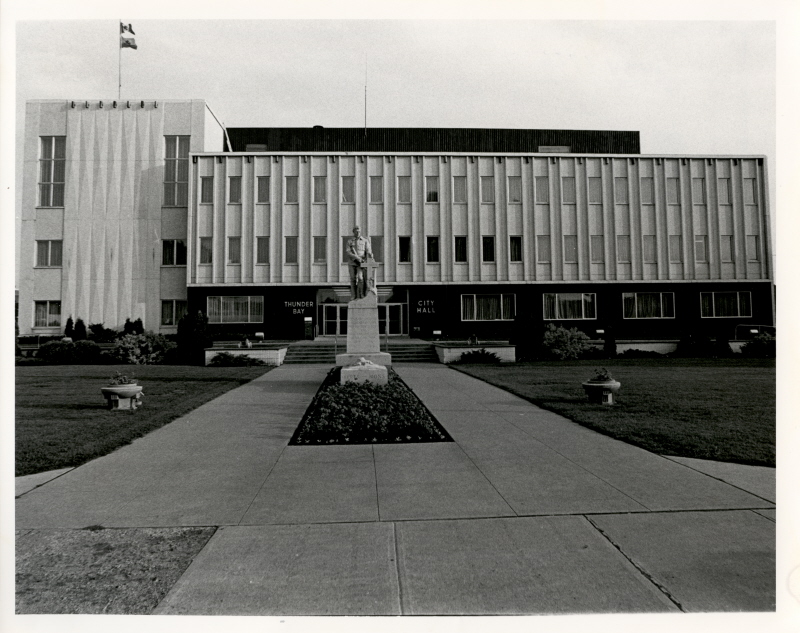 A front view of city hall with manicured lawns and a statue