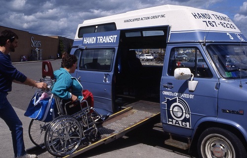 a person helping another person in a wheelchair enter a blue and white accessible van