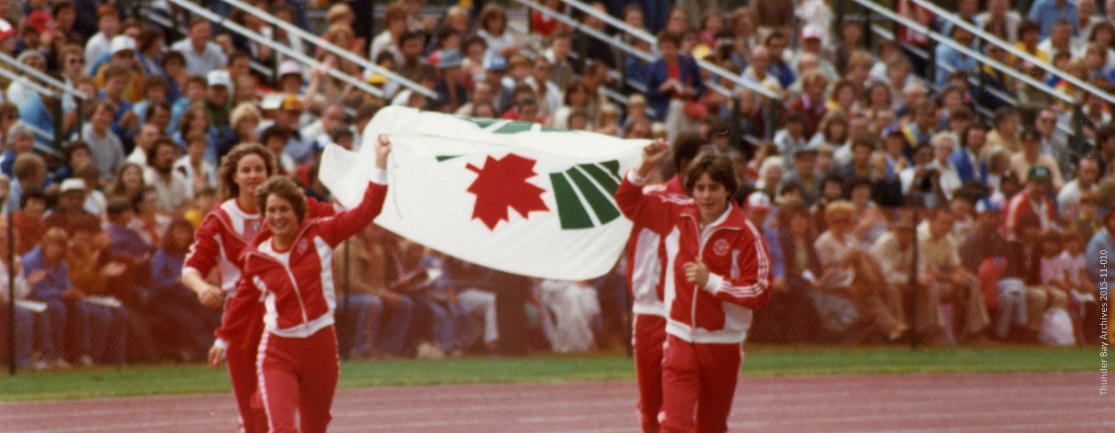 A group of athletes wearing red run with a flag held between the lead pair