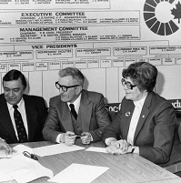 A group of people sitting around a table ready to sign a paper