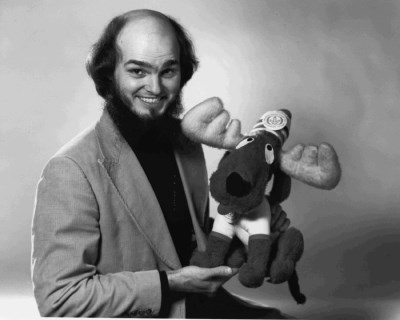 A man wearing a suit and tie holds a moose puppet 