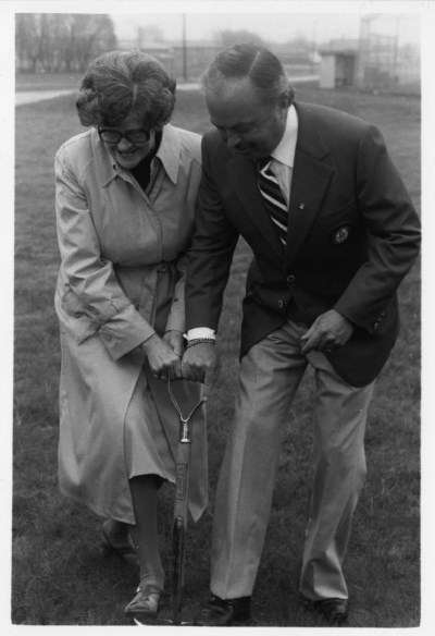 A man and a woman holding a shovel together while pushing it in the ground