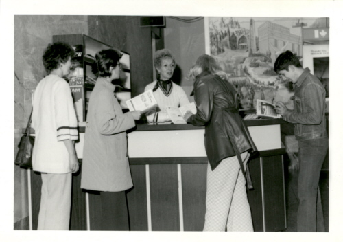 A group of people standing around a desk with a painting in the background