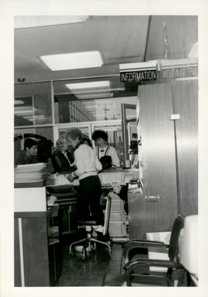 Two women standing behind a desk marked above with an information sign