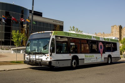 a bus sits out front of a glass front building with flags in the foreground