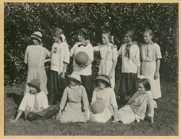 Ten girls posed outdoors for a team photograph with basketball and volleyball