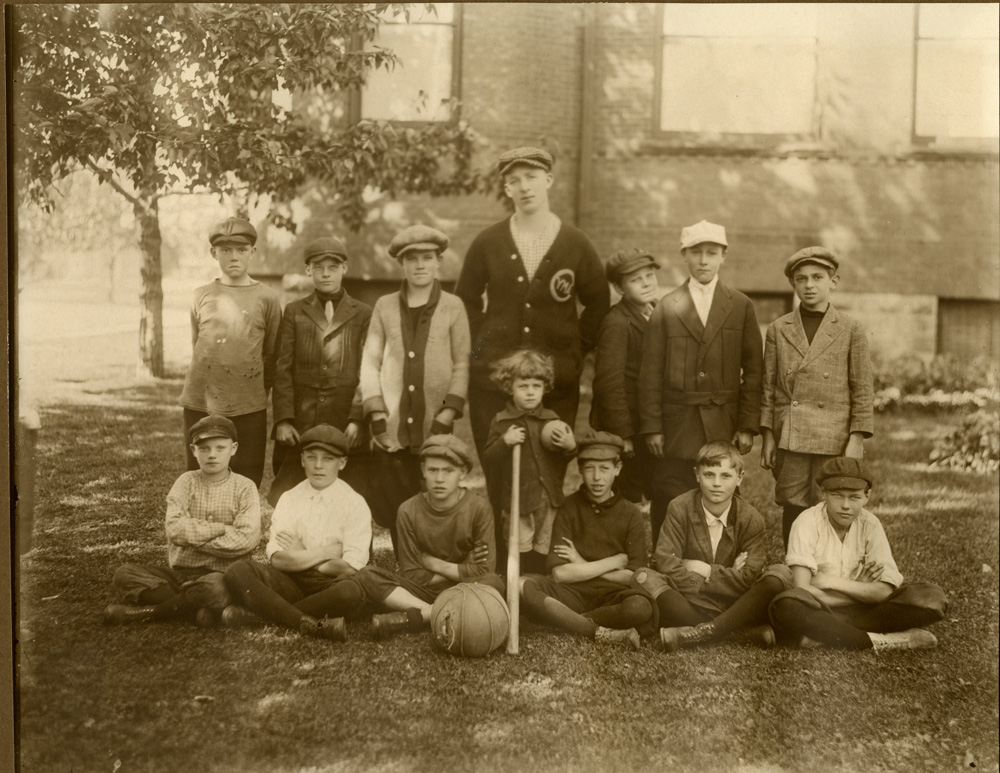 Boys sit and pose for a photograph with a ball and baseball bat