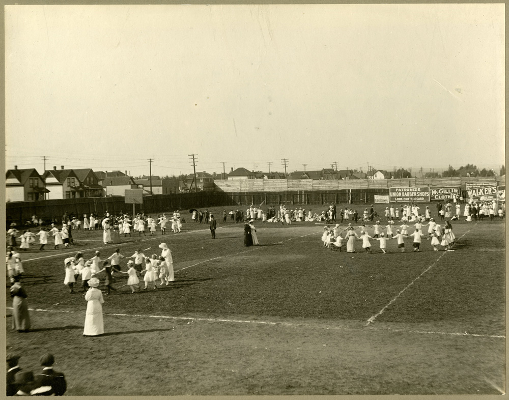 Preformers dance in a field while a crowd looks on 