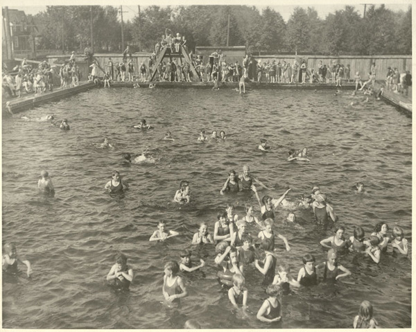 Numerous people in and around pool swimming and playing