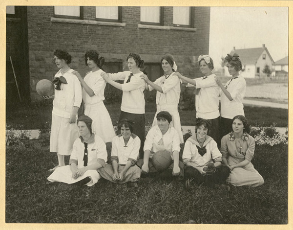 Outdoor team photograph of 11 girls posed with basketball and volleyball.