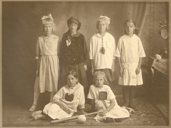 Six girls posed indoors for a team photograph with ball and bat.