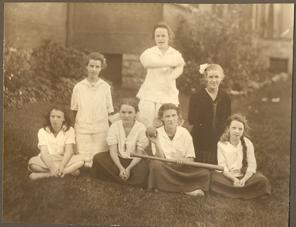 A team of seven girls posed outside with baseball equipment.