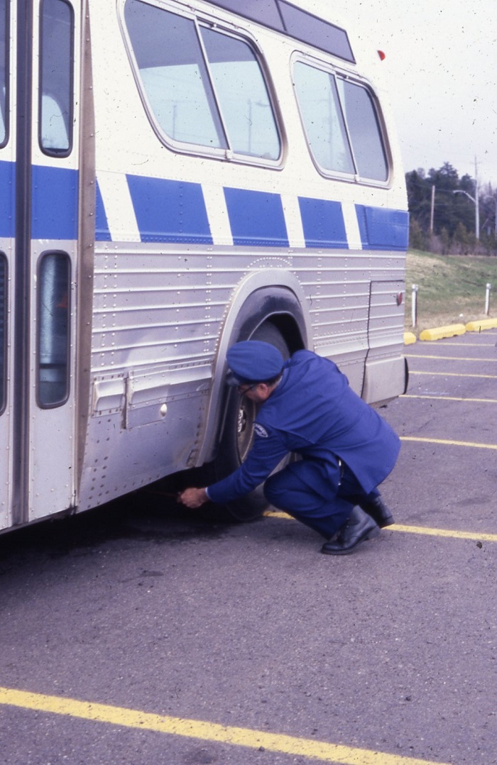 A person measuring the distance behind a bus wheel while squatting