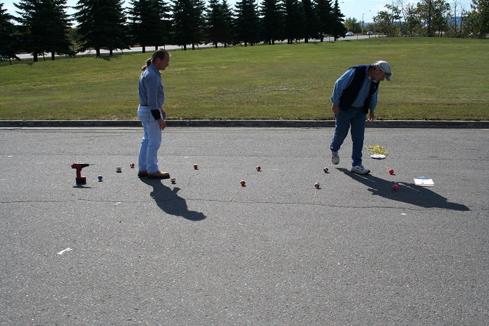 Two people placing coloured balls on the ground in a parking lot