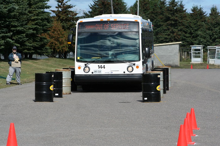 A bus being navigated through two rows of closely placed black barrels