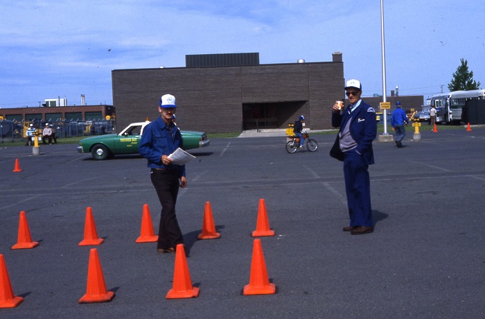 Two people standing with clipboards among a grouping of orange cones