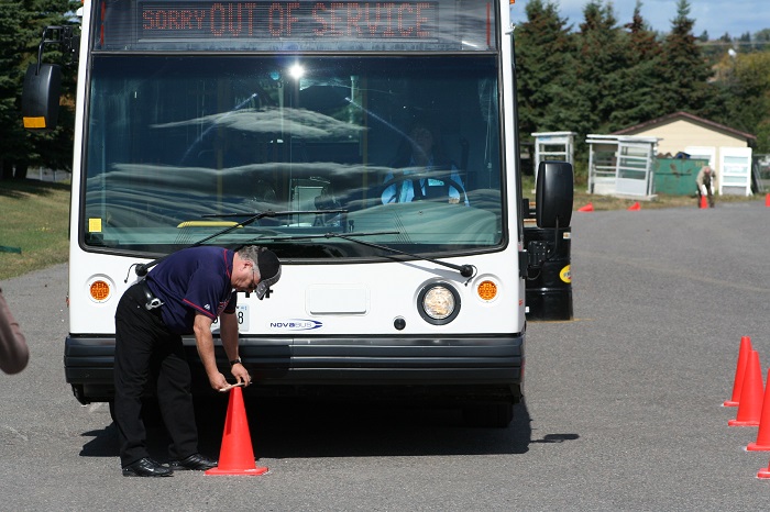 a man placing an orange traffic cone in front of an out of service bus
