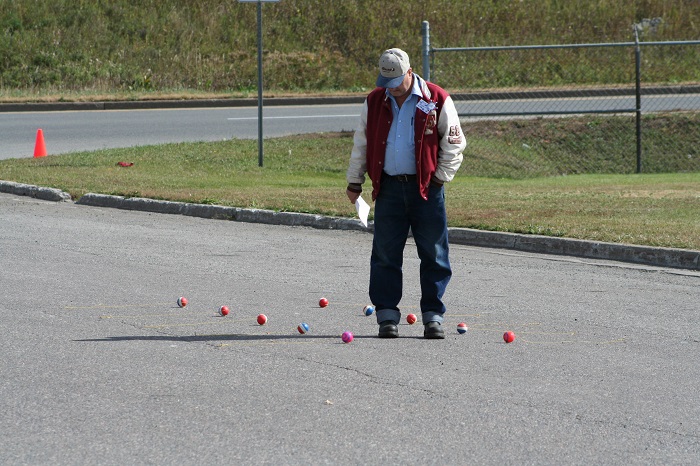 a man standing on a road looking down to check the location of small balls