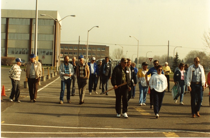 A group of people holding various rulers and clipboards walk down a road