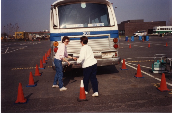 Two people standing in front of a bus as one person hands something to the other