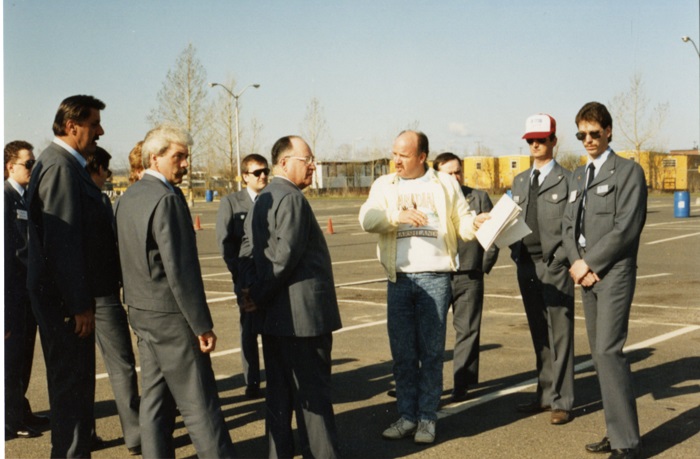 A group of people listening to a man holding a clipboard 