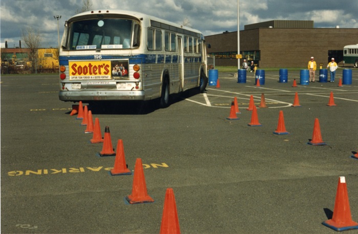 A bus navigating its way through orange pylons in an empty parking lot