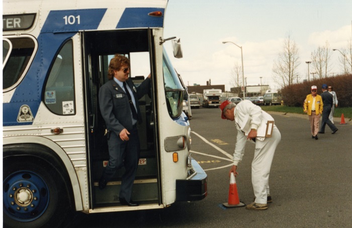 A driver stepping off a bus as a man places an orange cone in front