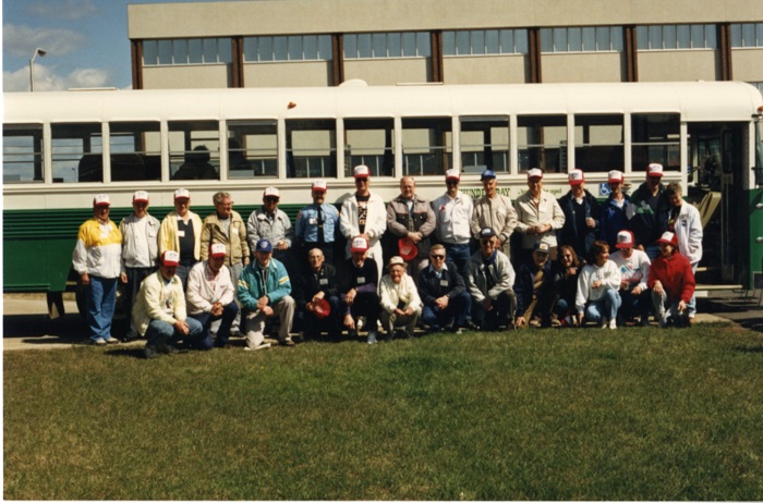 A group of people standing and sitting in front of a green and white bus