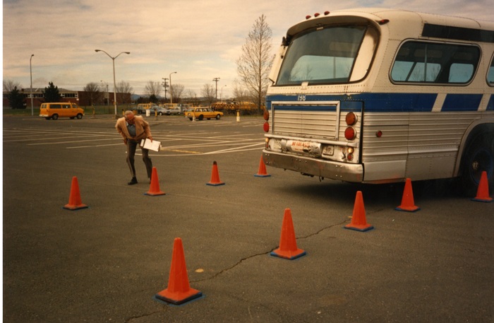 A bus backing up between two rows of equi-distant orange cones
