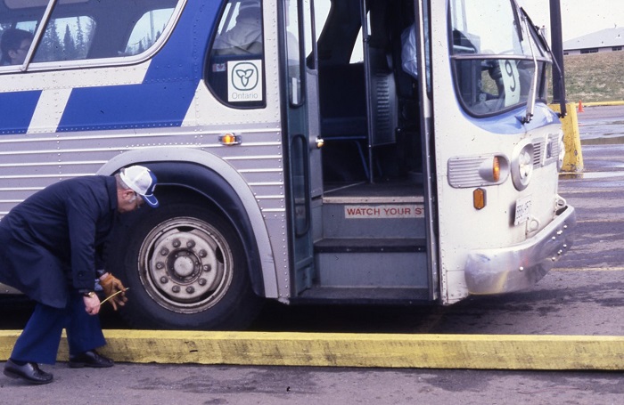 A person measuring the distance between a curb and the wheel of a parked bus
