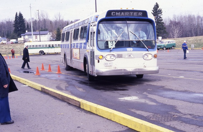 A bus pulling up to the curb after passing by a row of orange cones