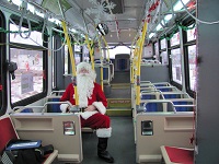 Santa sits alone on a bus decorated with snowflakes and garland