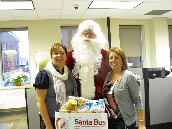Santa with two city employees showing off the full donation bin