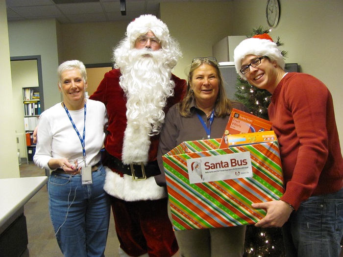 Santa, his helper, and two others showing off the full donation bin in City Hall