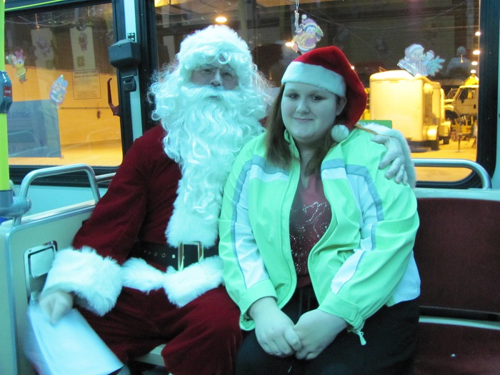 Santa sitting on the bus with a person wearing a santa hat beside him
