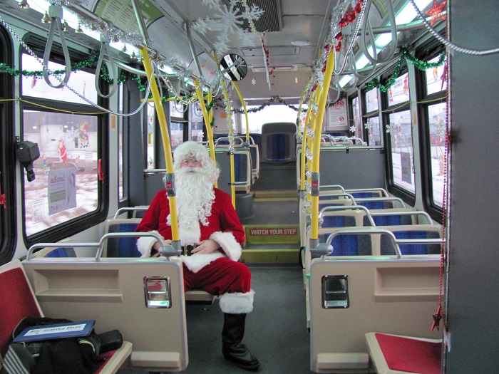 Santa sitting by himself on a bus decorated with snowflakes and garland